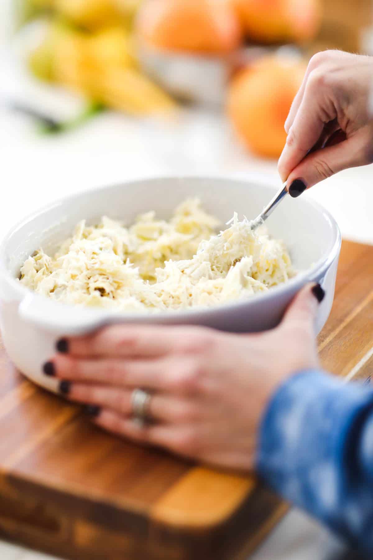 Woman stirring ingredients for a hot artichoke dip in a baking dish.