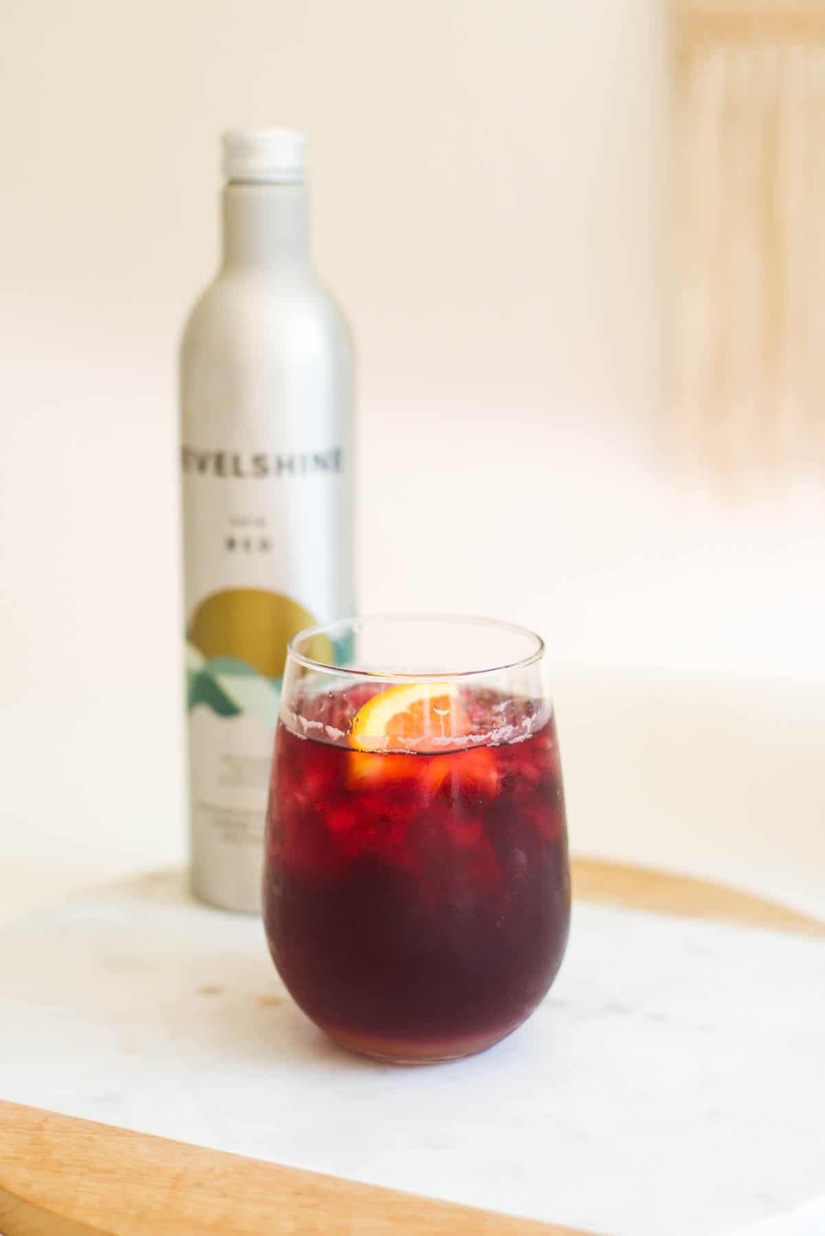 A stemless wine glass with a cocktail next to a bottle on a table.