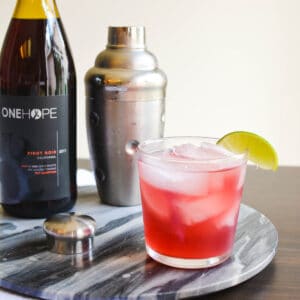 Close up of a tequila cocktail on a tray next to a cocktail shaker and wine bottle.