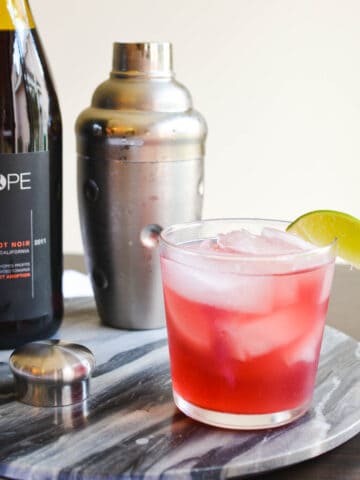 Close up of a tequila cocktail on a tray next to a cocktail shaker and wine bottle.