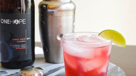 Close up of a tequila cocktail on a tray next to a cocktail shaker and wine bottle.