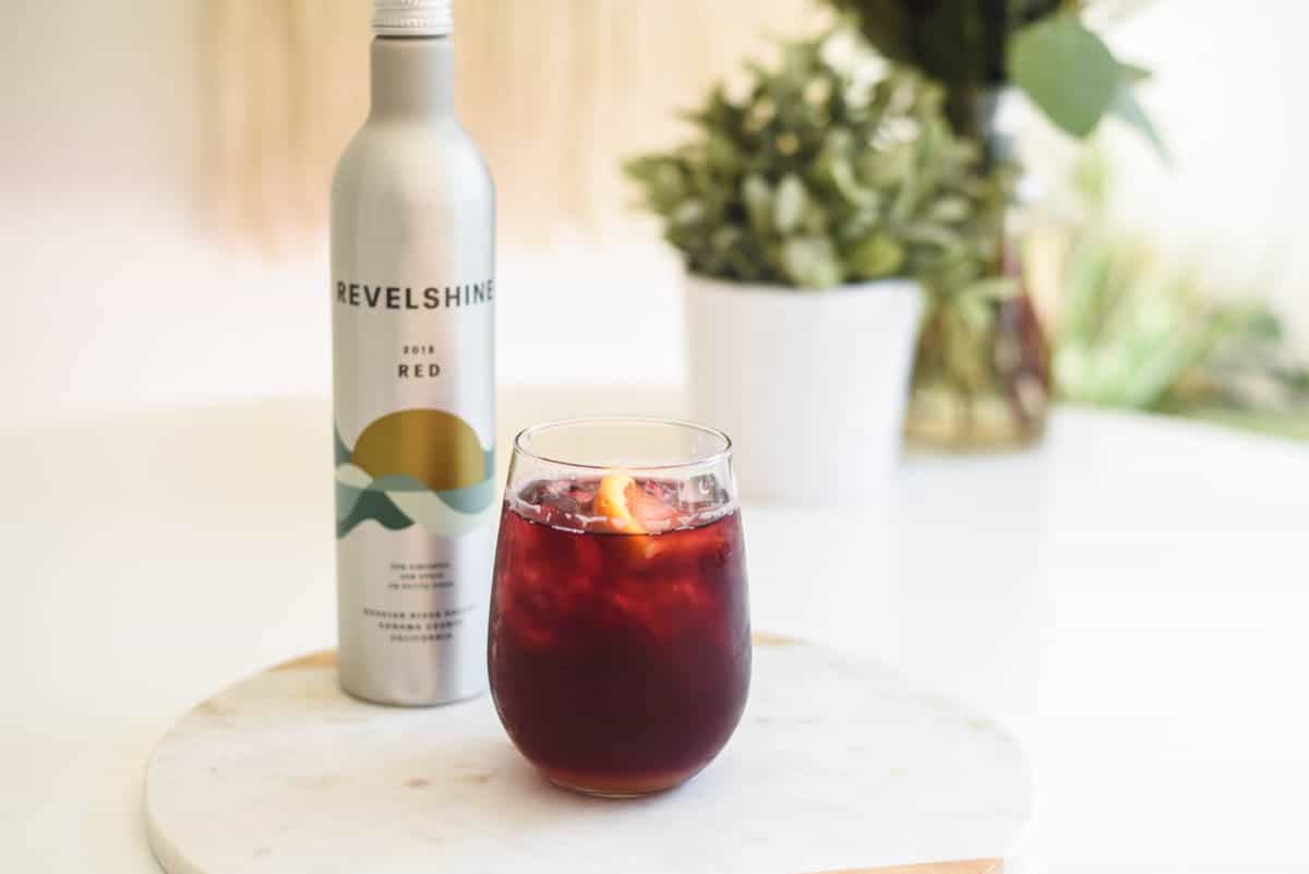 Red wine in a glass on a table next to a small aluminum bottle of wine.