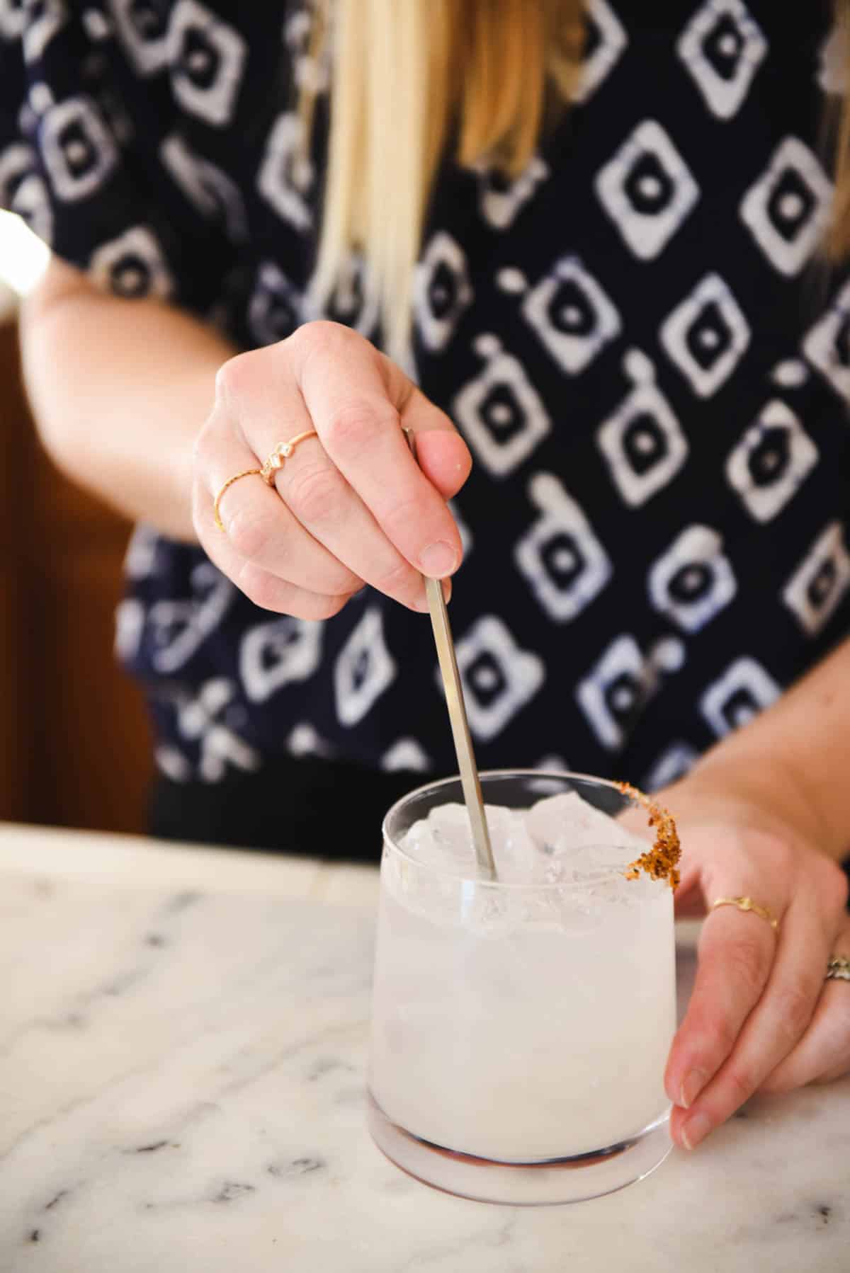 Woman stirring a basil margarita with with a bar spoon on the counter.