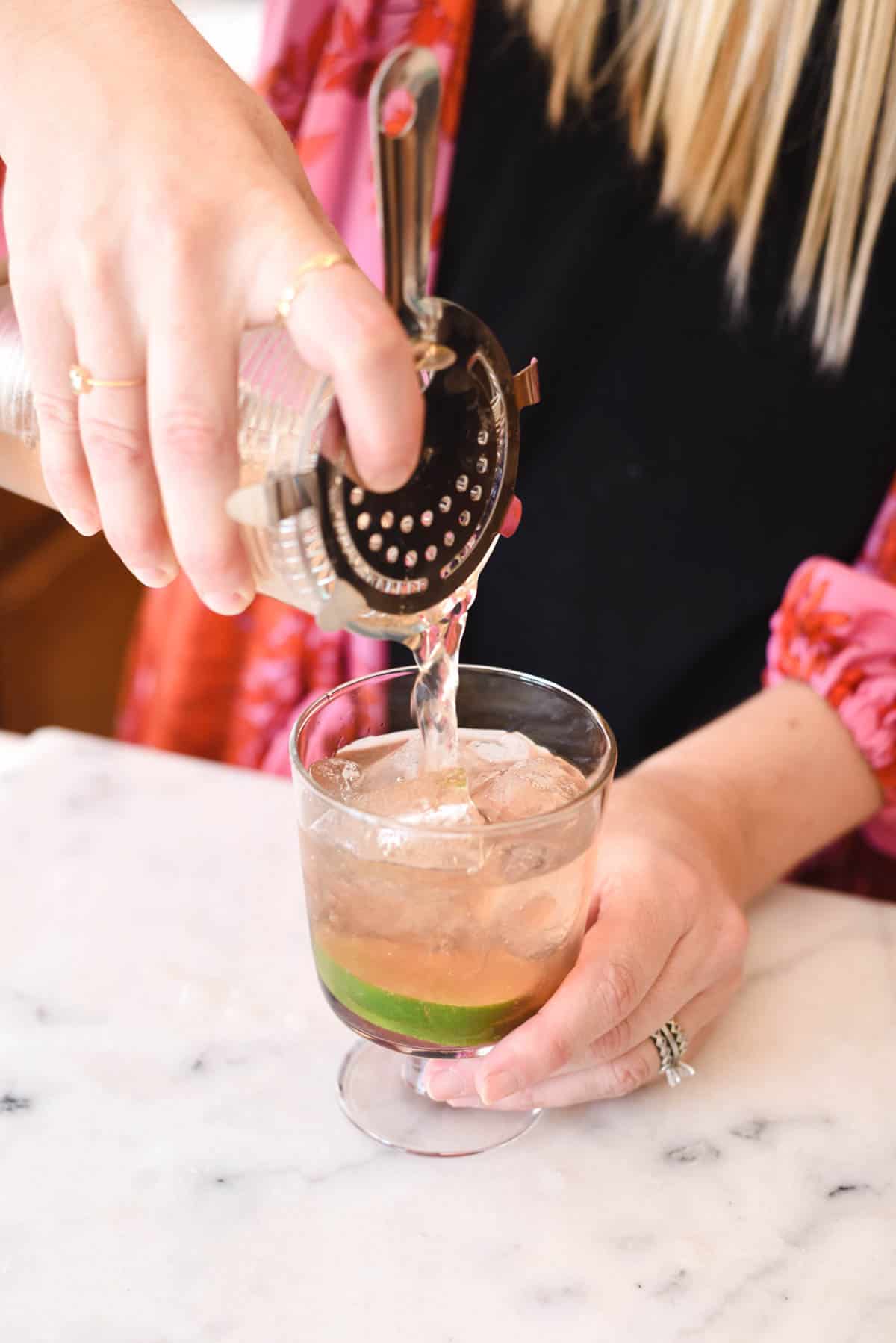 Woman pouring a cocktail in to a glass with a cocktail strainer.