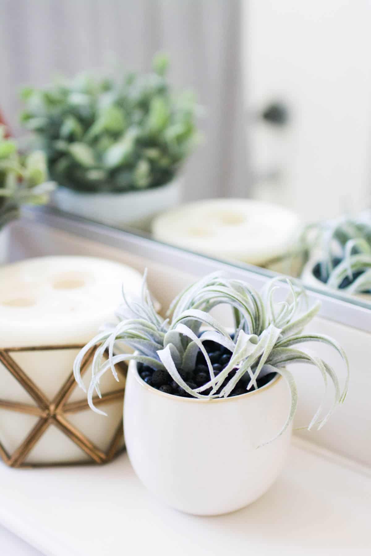 A water free diffuser made with lava rocks and a faux succulent next to a candle.