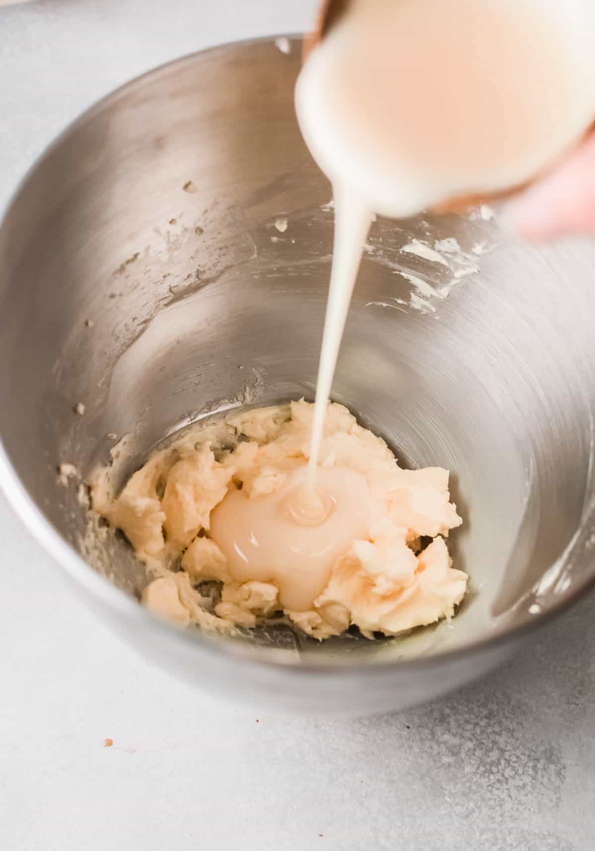 Condensed milk being poured into butter in mixing bowl. 