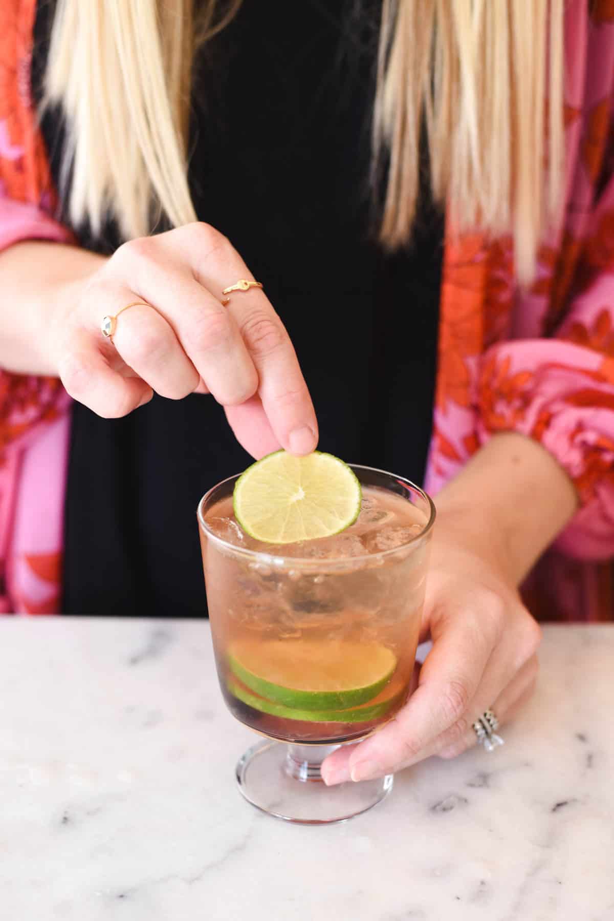 Woman adding a lime slice to the top of a cocktail.