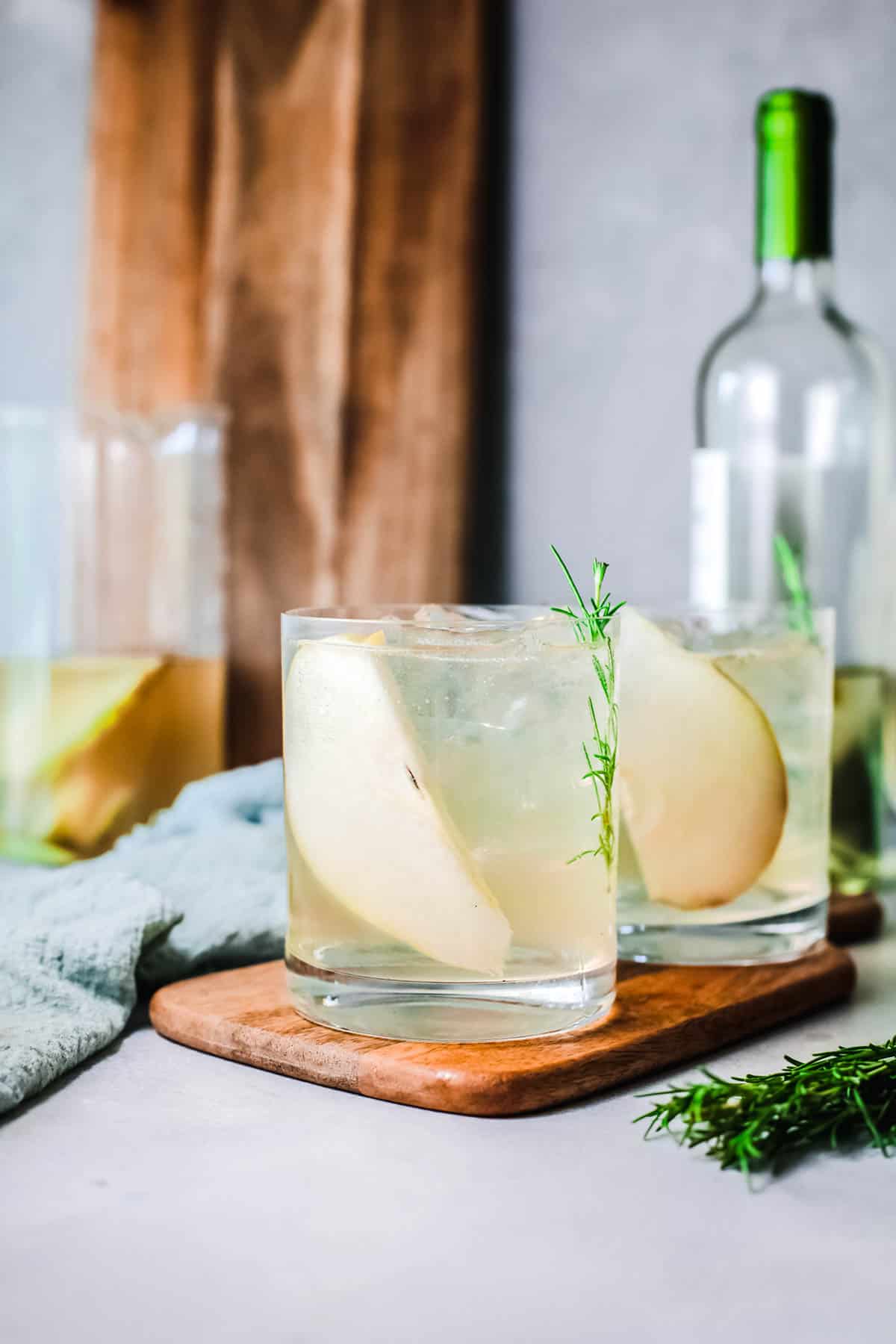 Side view of cocktail glasses on a tray with pear and rosemary garnish.