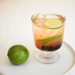 Close up of a cocktail glass sitting next to a lime on a table.