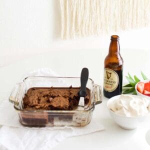 A glass baking dish with beer brownies next to a small bowl of whipped cream and Guinness beer.