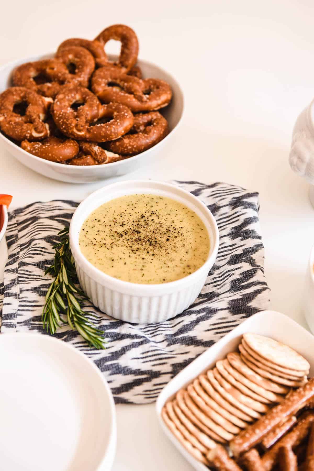 A small white bowl with hot beer cheese dip next to bowls of crackers and pretzels.