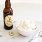Square image of a bowl with beer whipped cream, a bottle of Guinness stout and a spoon.