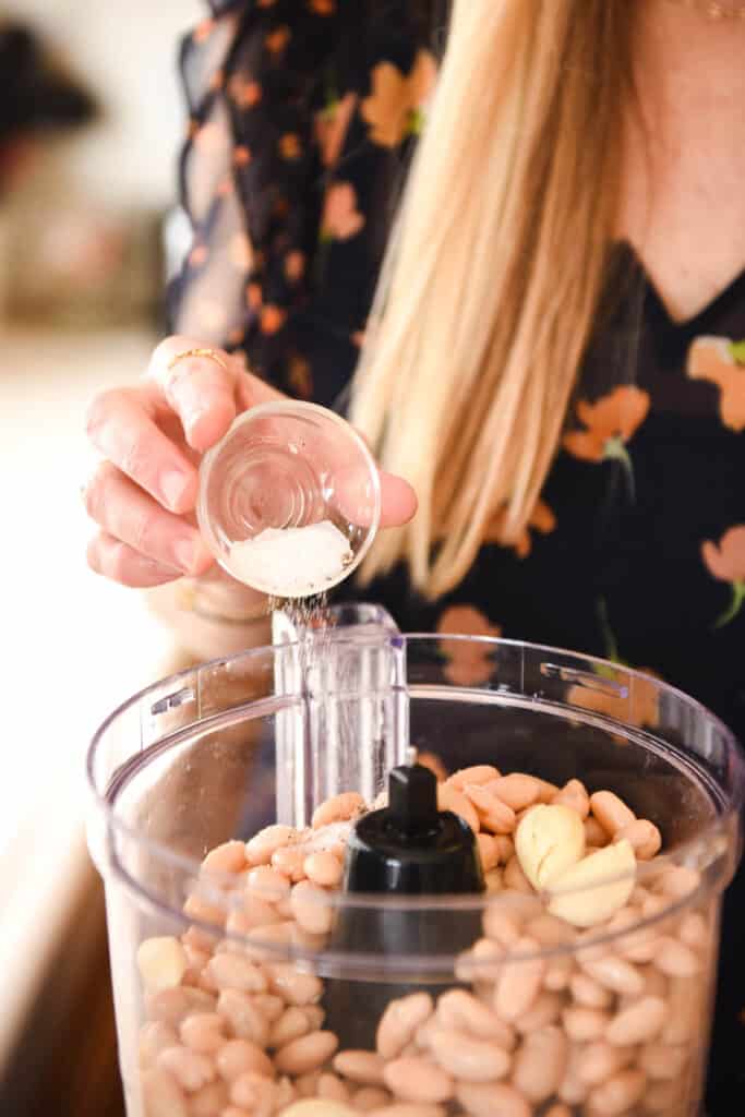Woman adding salt and pepper to a recipe in a food processor.