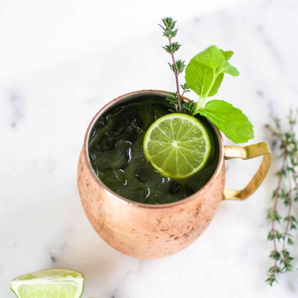 Close up of a copper mug holding a Green Moscow Mule cocktail with herb garnish.