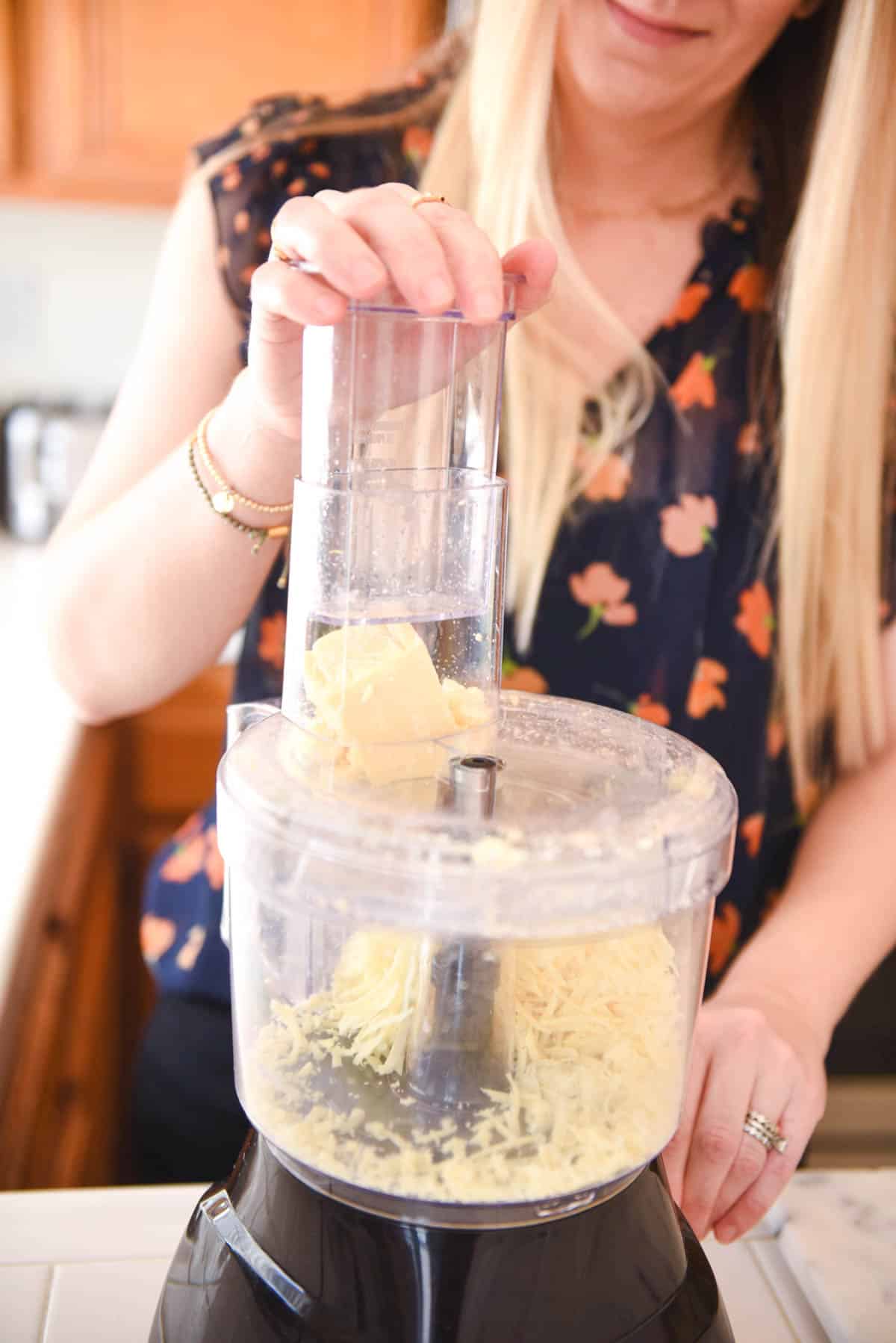Woman using a food processor to grate cheese.