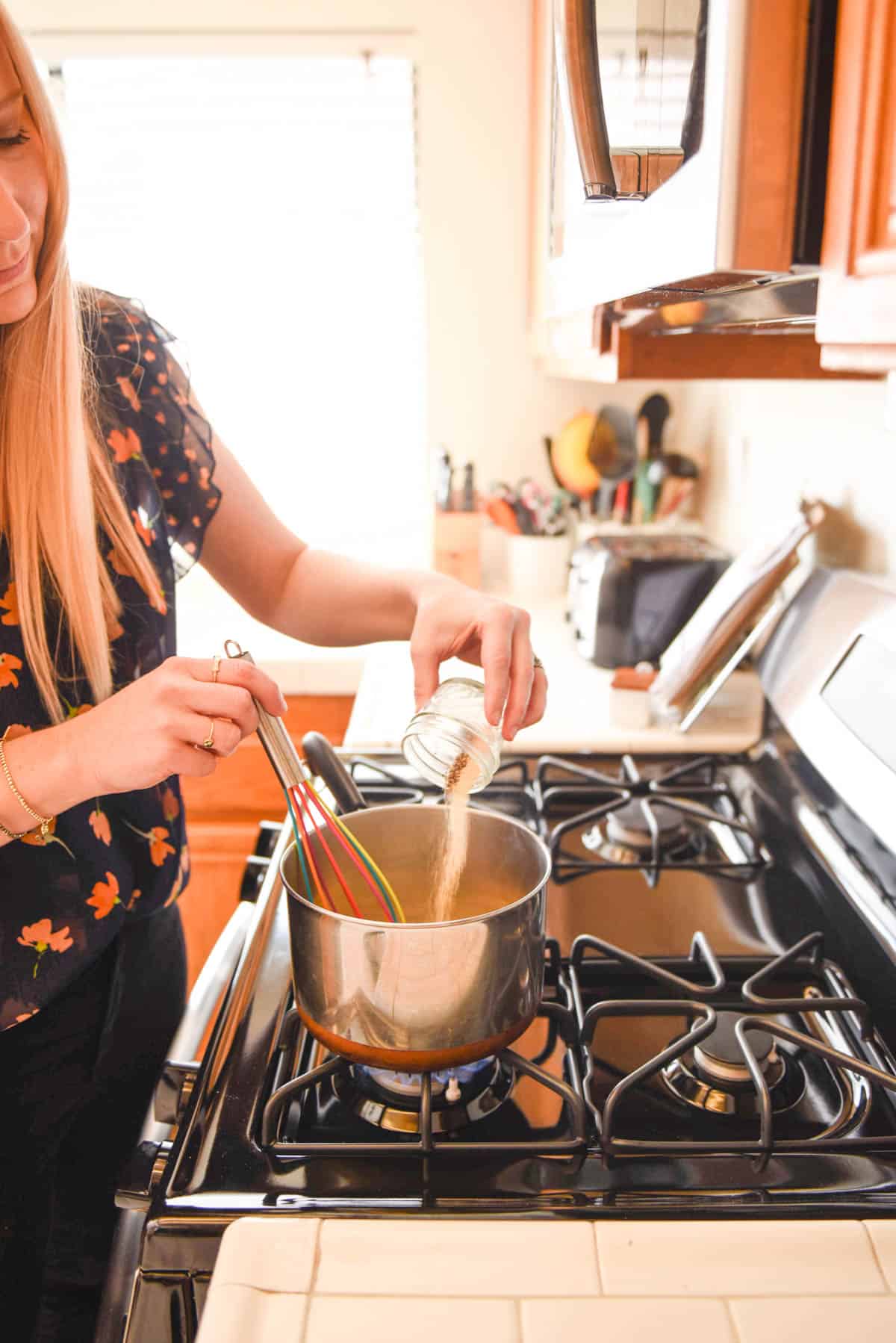 Woman adding spices to a saucepan on the stove.