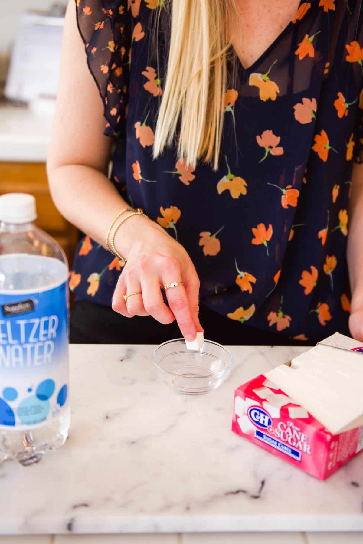 Woman adding one sugar cube to a small glass bowl on a counter.