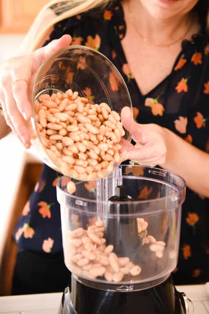 Woman adding white beans to a food processor.