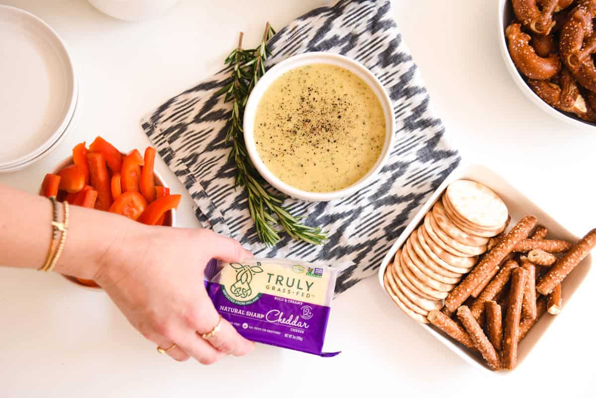 Beer Cheese Dip in a small white bowl on the table next to a girl holding a package of cheese.