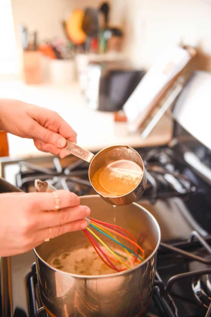 Woman adding beer from a measuring cup to a saucepan on the stove.