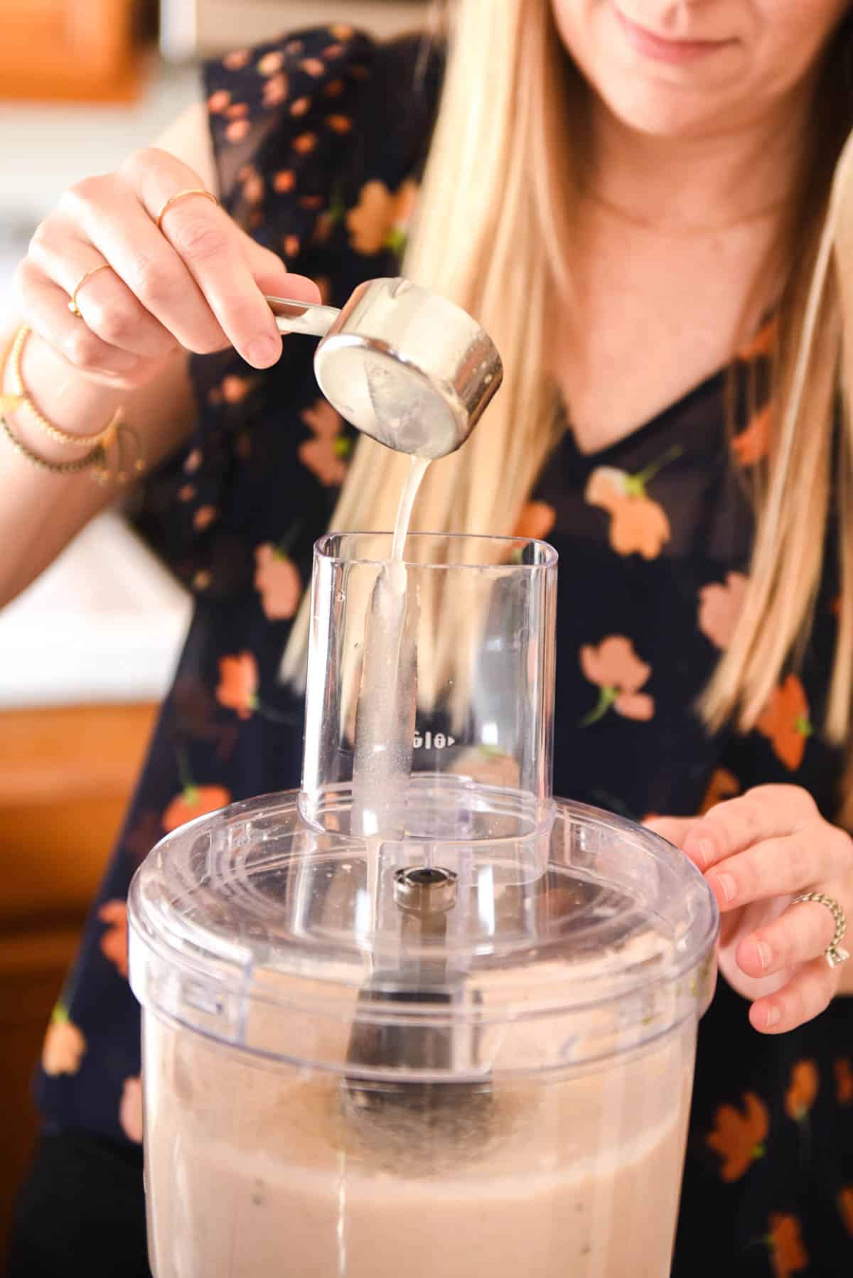 Woman using a measuring cup to add liquid to a food processor.