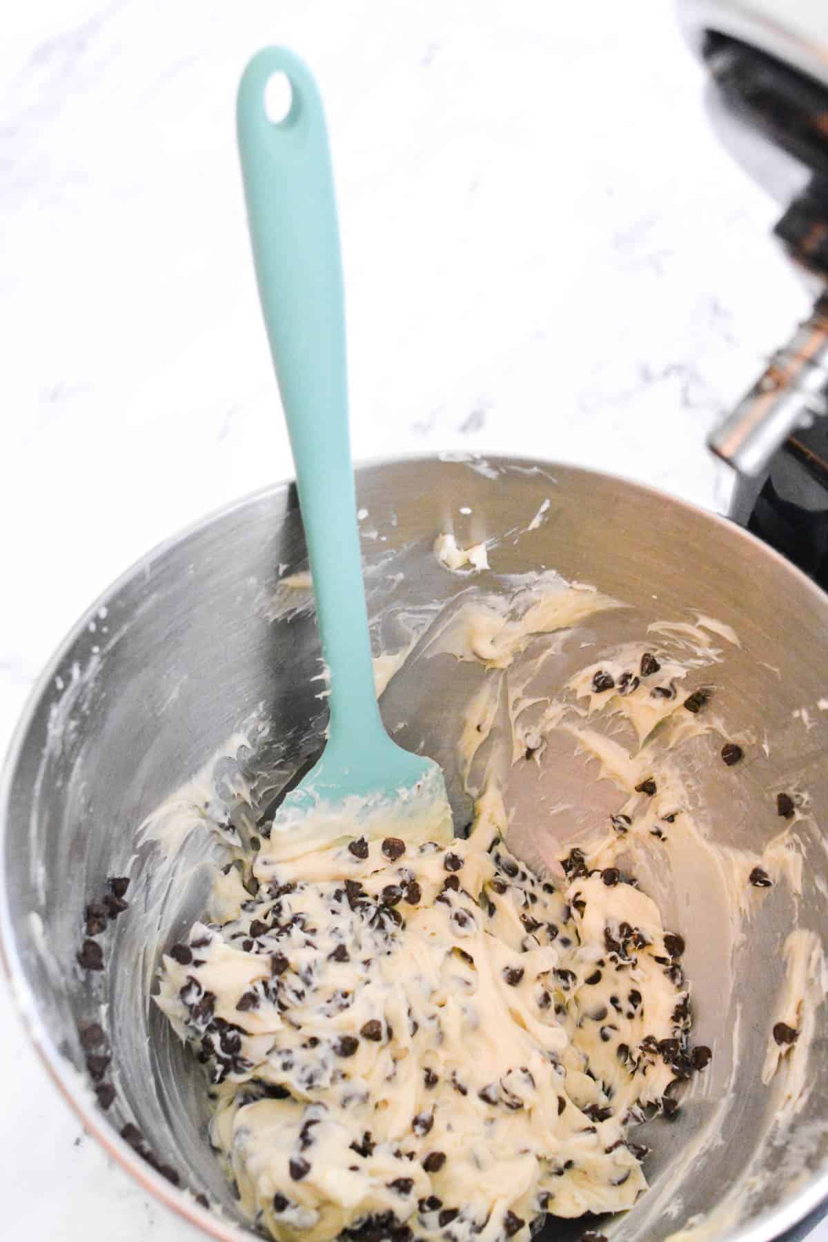 A bowl of a stand mixer with a dessert dip with chocolate chips and a spatula in the bowl.