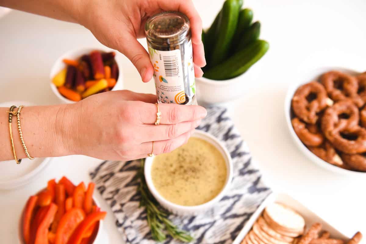 Woman cracking black pepper on the top of hot beer cheese dip.