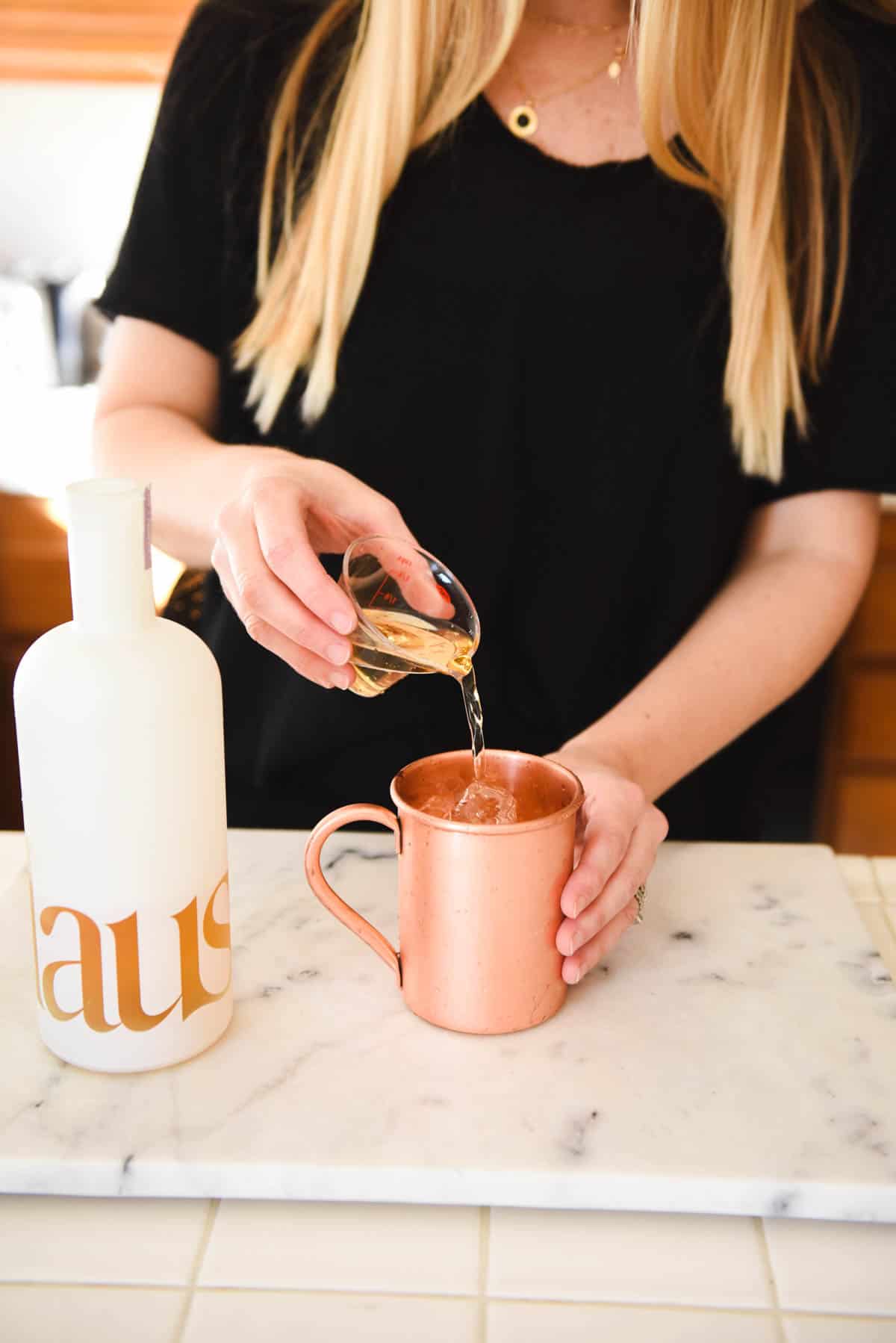 Woman adding Haus to a copper mug on a counter.