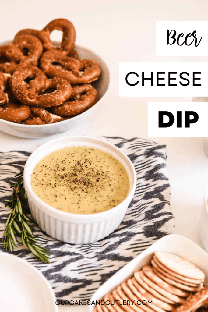 A white bowl of hot beer cheese dip on a table next to a bowl of pretzels and crackers.