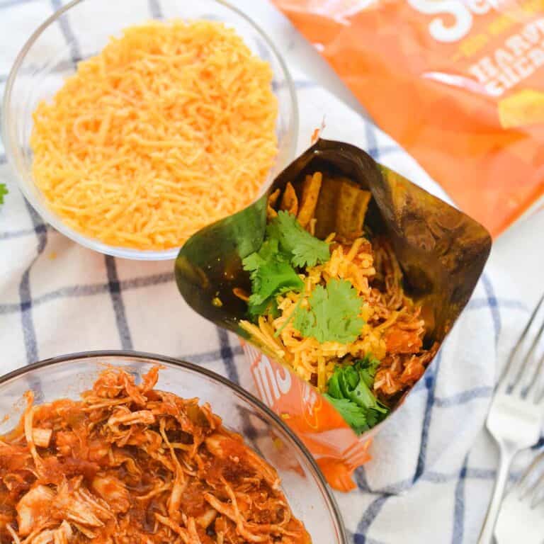 Close up of a bag of chips topped with shredded chicken for walking tacos.