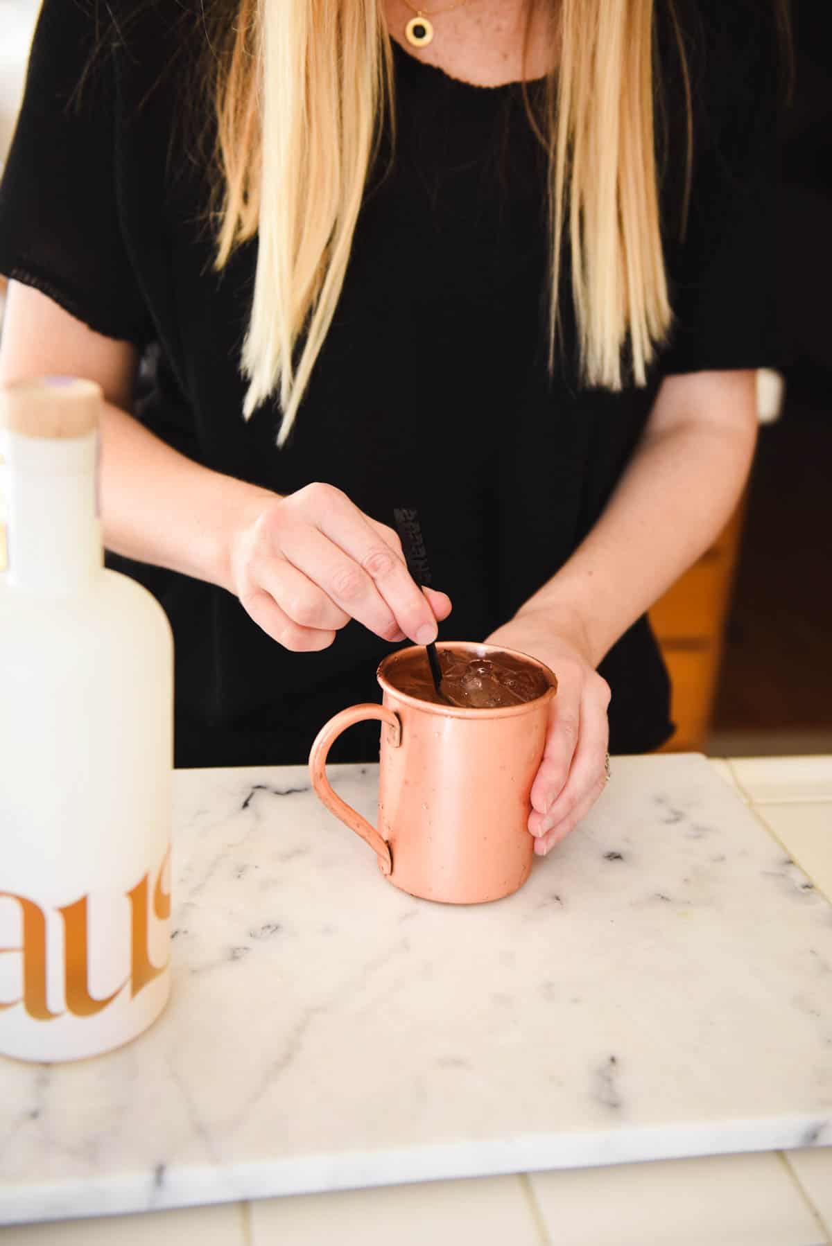 Woman stirring a cocktail in a copper mug on the counter.