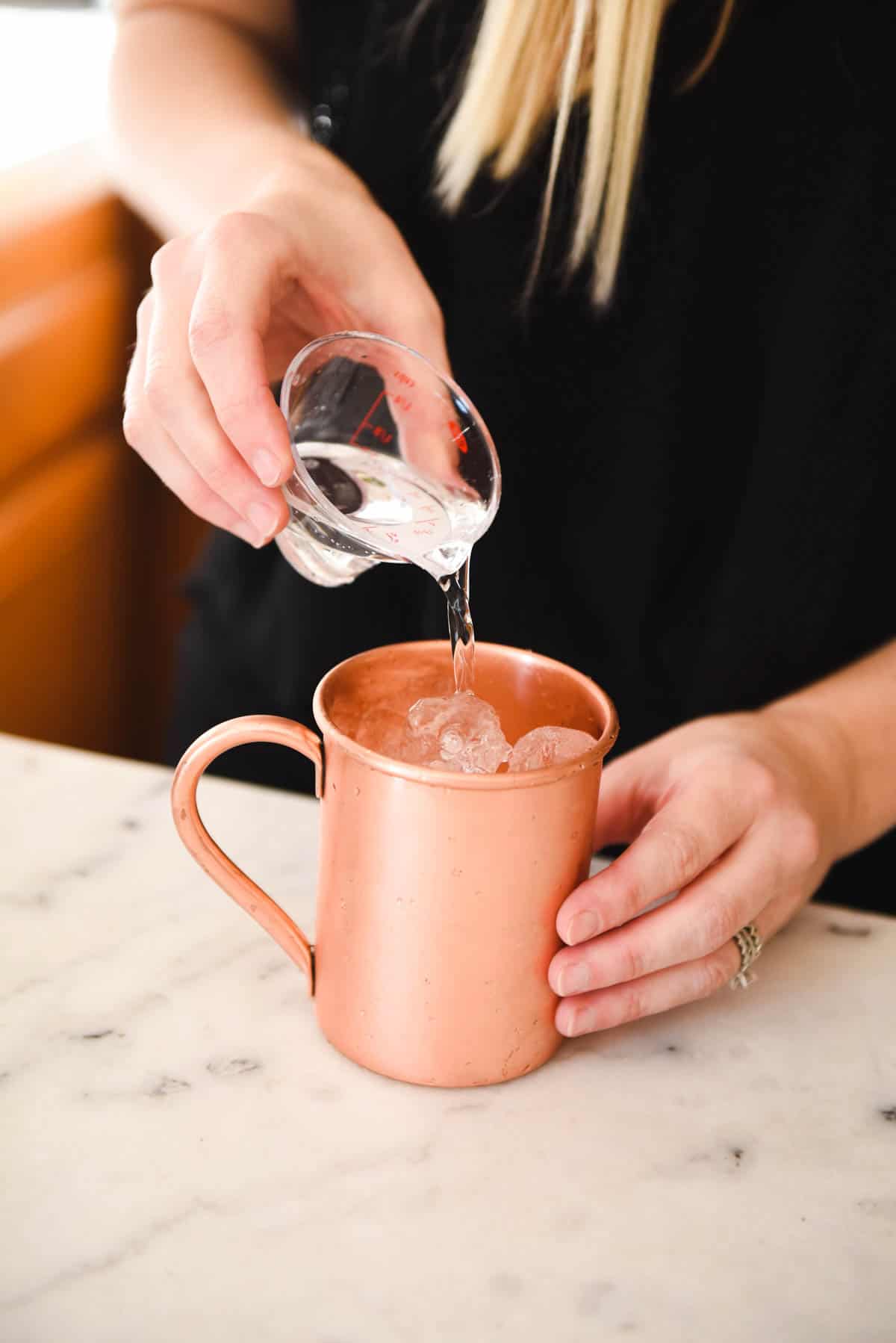 Woman adding vodka to a copper mug on a counter.