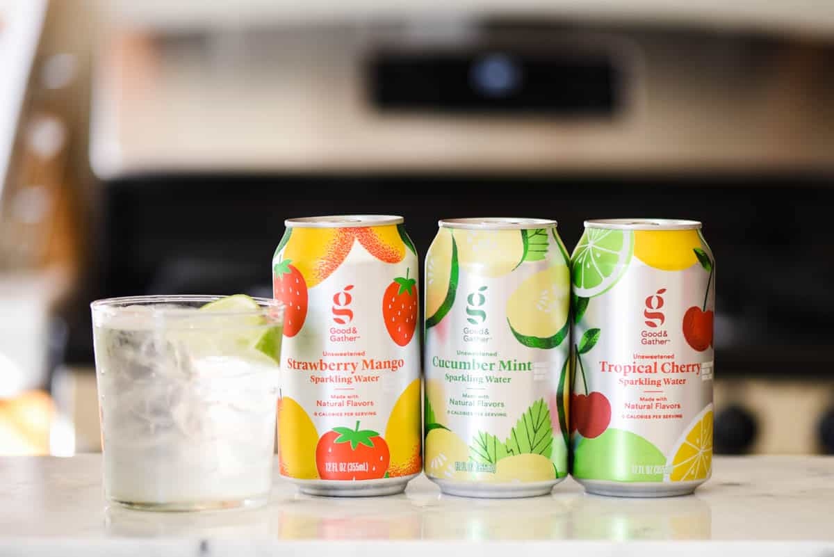 Flavored sparkling waters on a counter next to a glass.