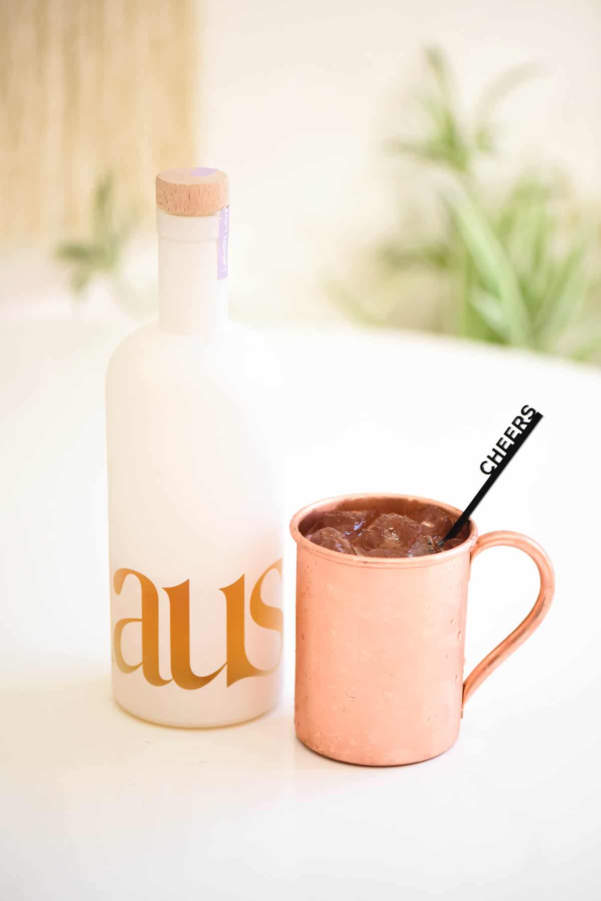 A bottle of Lemon Lavender Haus on a table next to a copper Moscow Mule mug.