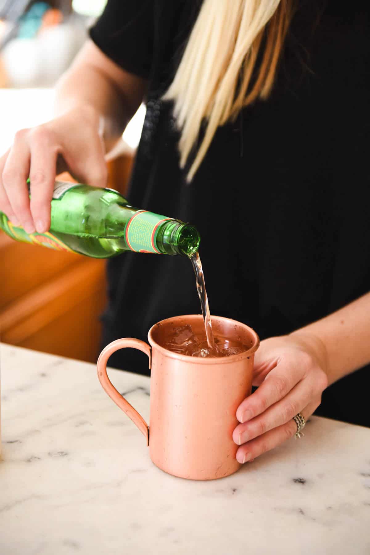 Woman pouring ginger beer into a copper mug on a counter.