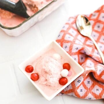 Top down image of a small square dish filled with homemade strawberry ice cream made with condensed milk topped with candy next to a spoon and napkin.