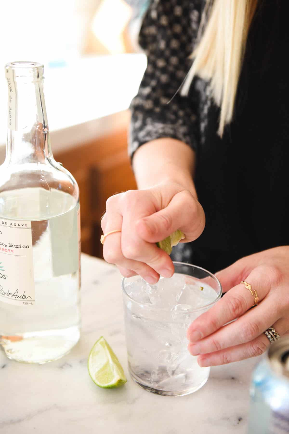 Woman squeezing lime into a tequila cocktail.