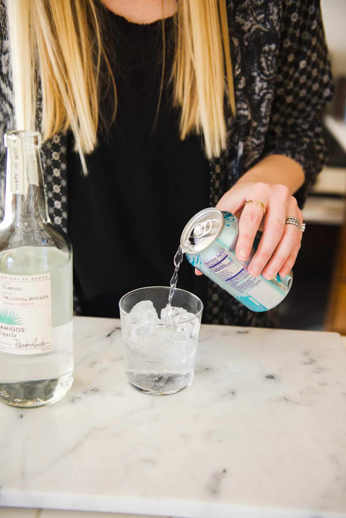 Woman adding club soda to a glass on a counter.