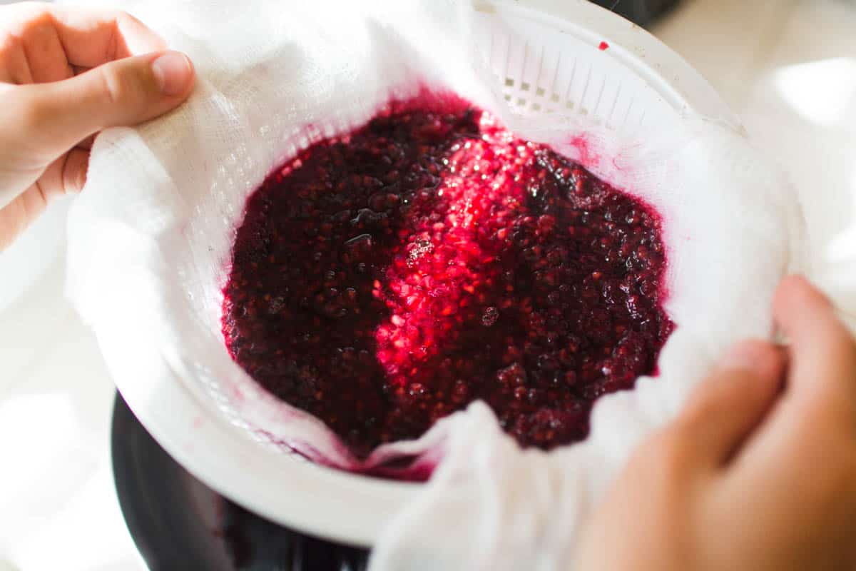 Straining blackberry cocktail syrup into a bowl through cheesecloth. 