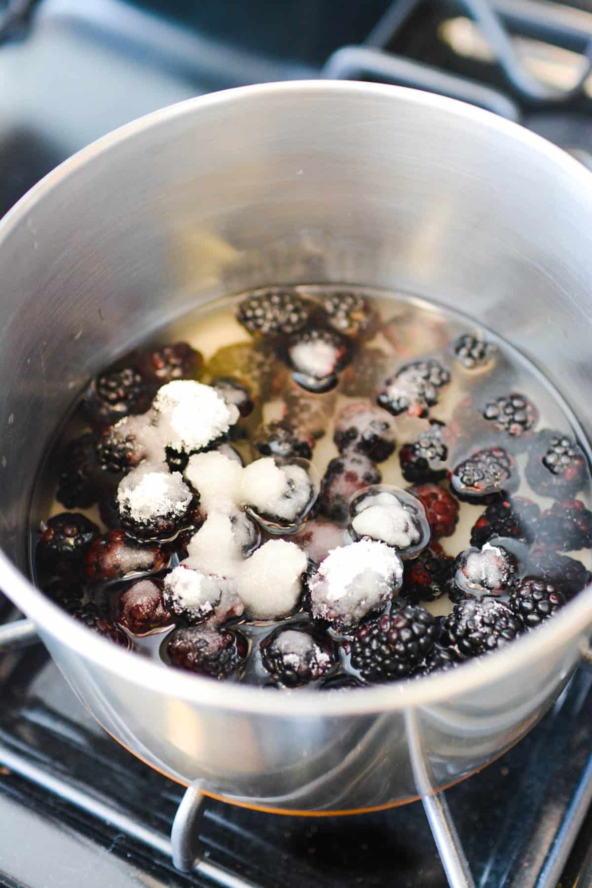 Heating blackberries, sugar and water in a pan on the stove.