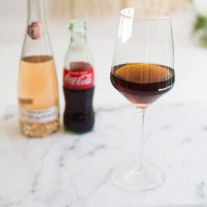 A stemmed wine glass with coke and wine on a table.