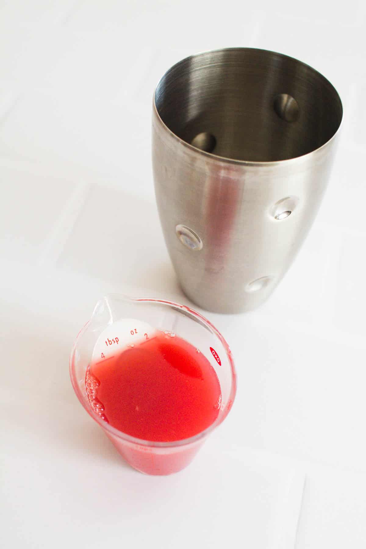 Blood orange juice in a measuring cup next to a cocktail shaker.