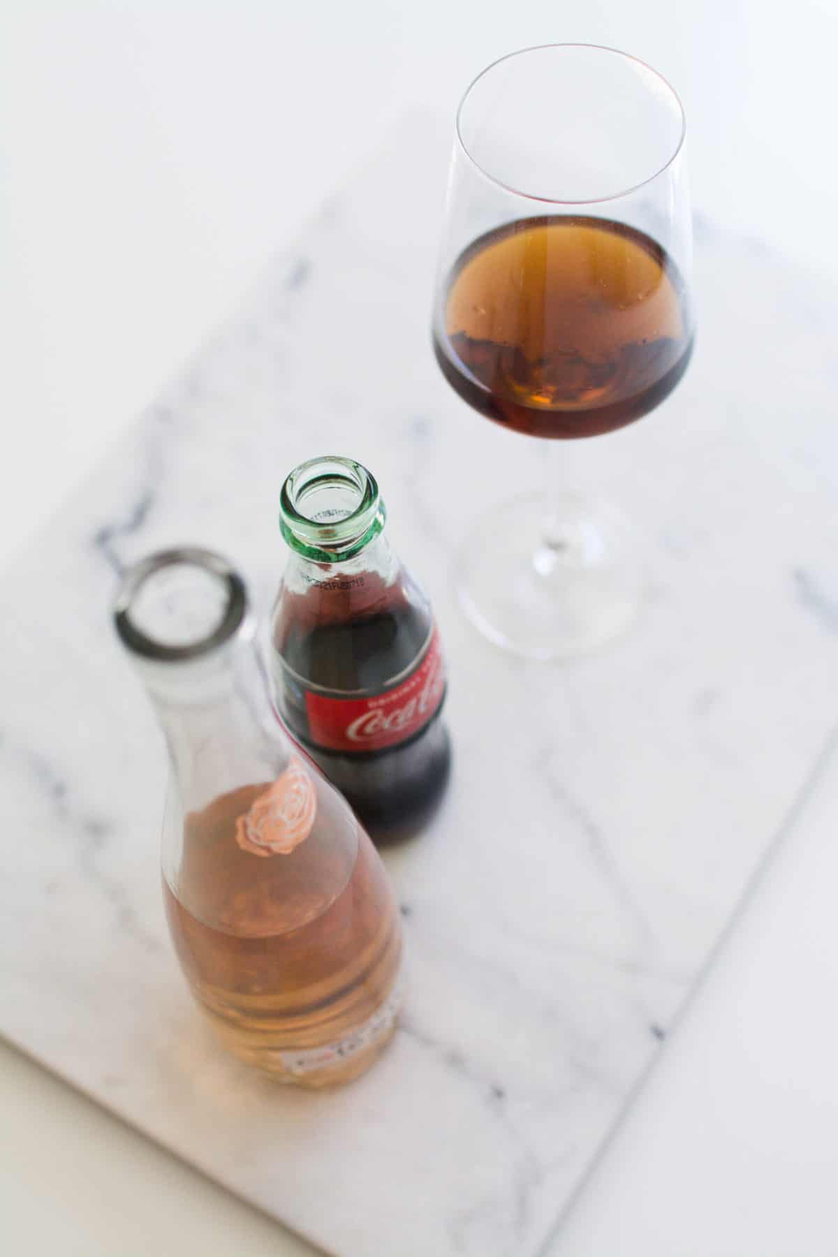 Overhead shot of a cutting board with a bottle of wine and a coke next to a wine glass.