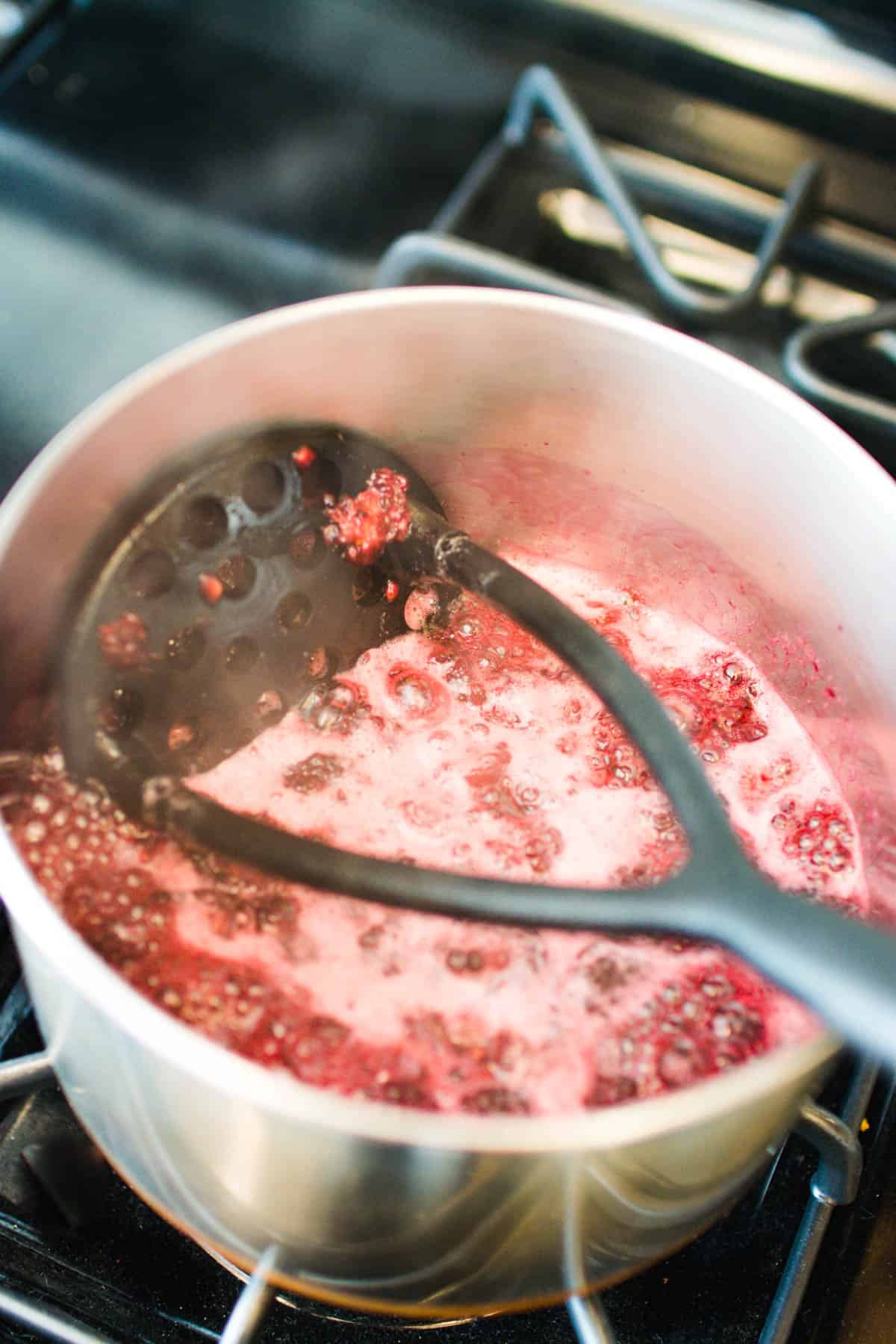 Mashing up blackberries once they've cooked down on the stovetop.