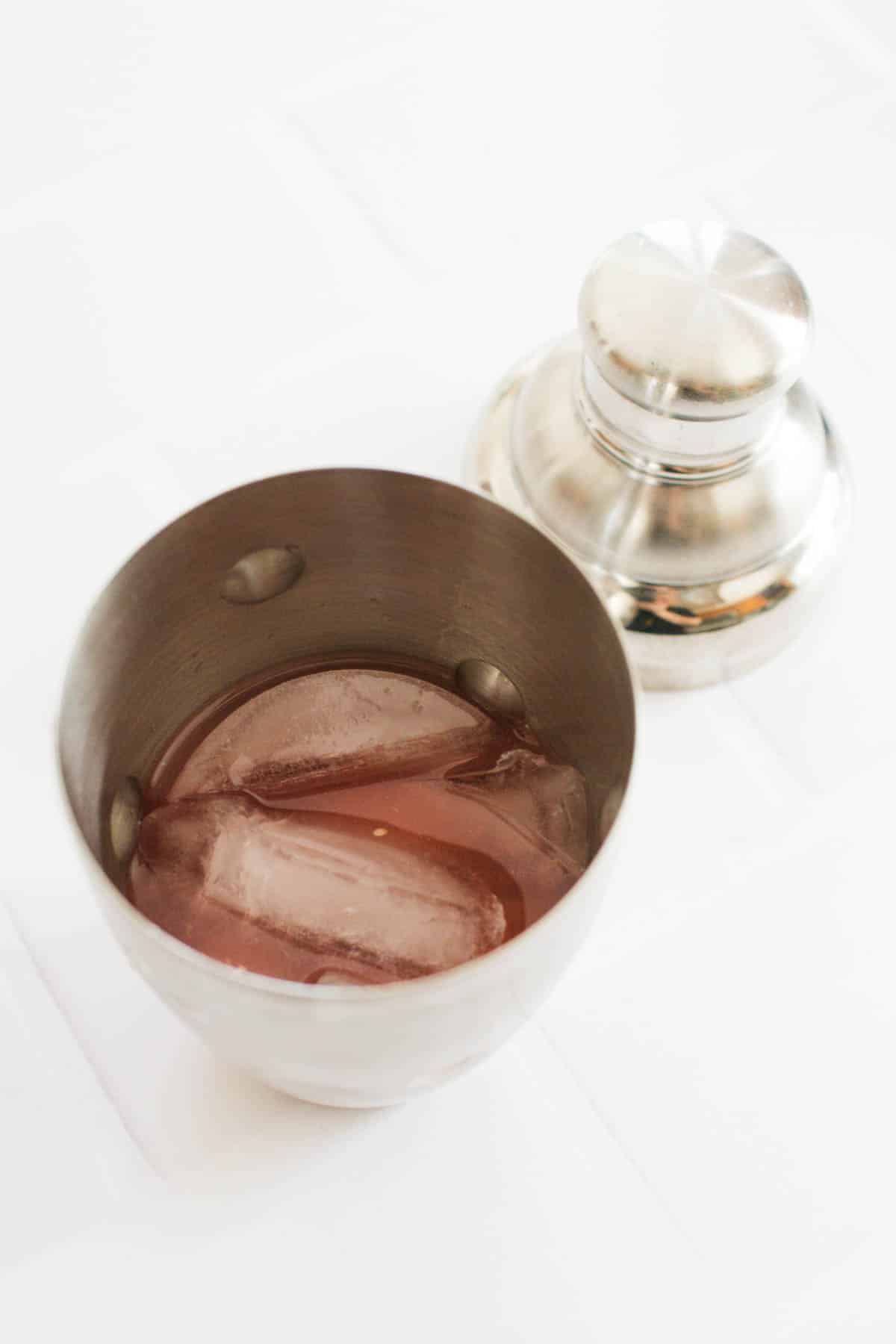 A cocktail shaker with ice and blood orange juice on a counter.