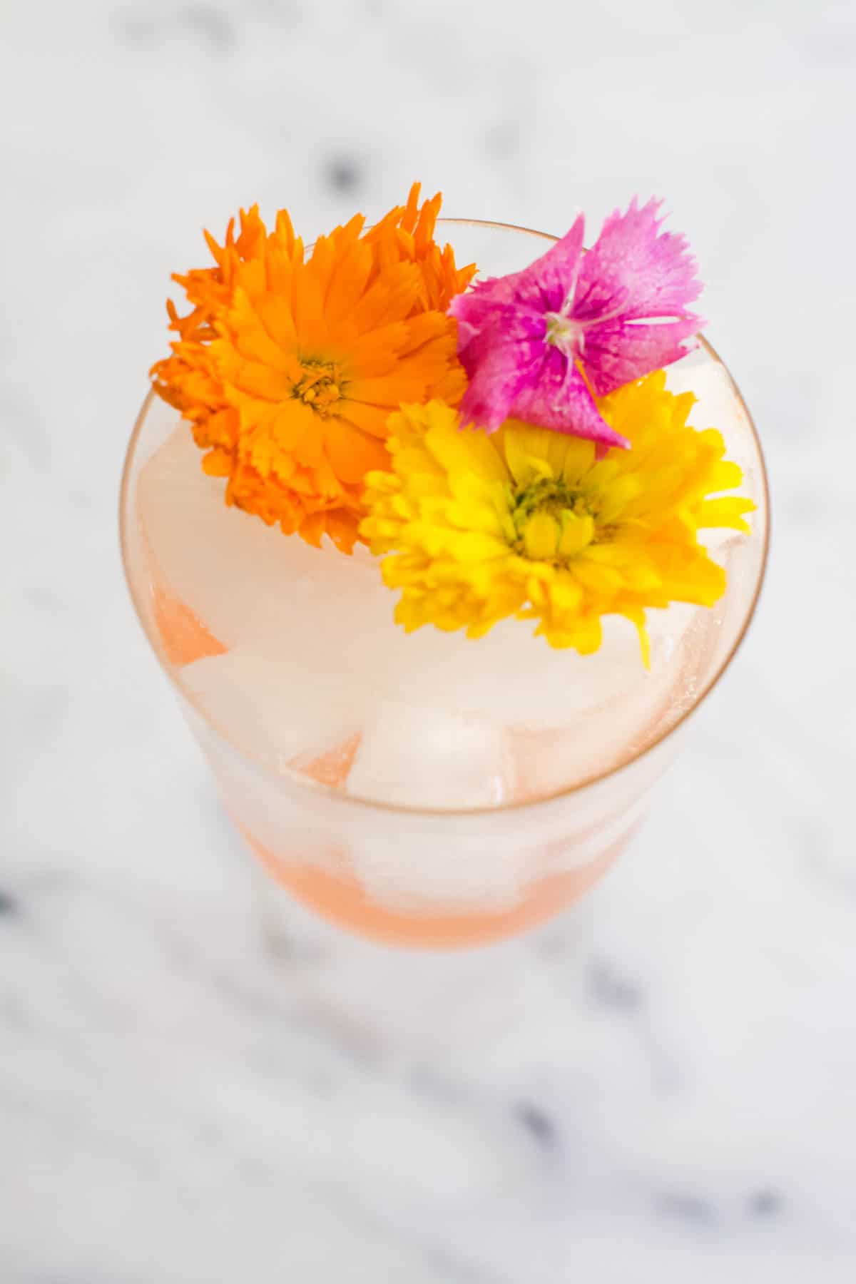 Close up of edible flowers in a stemmed wine glass on a table.