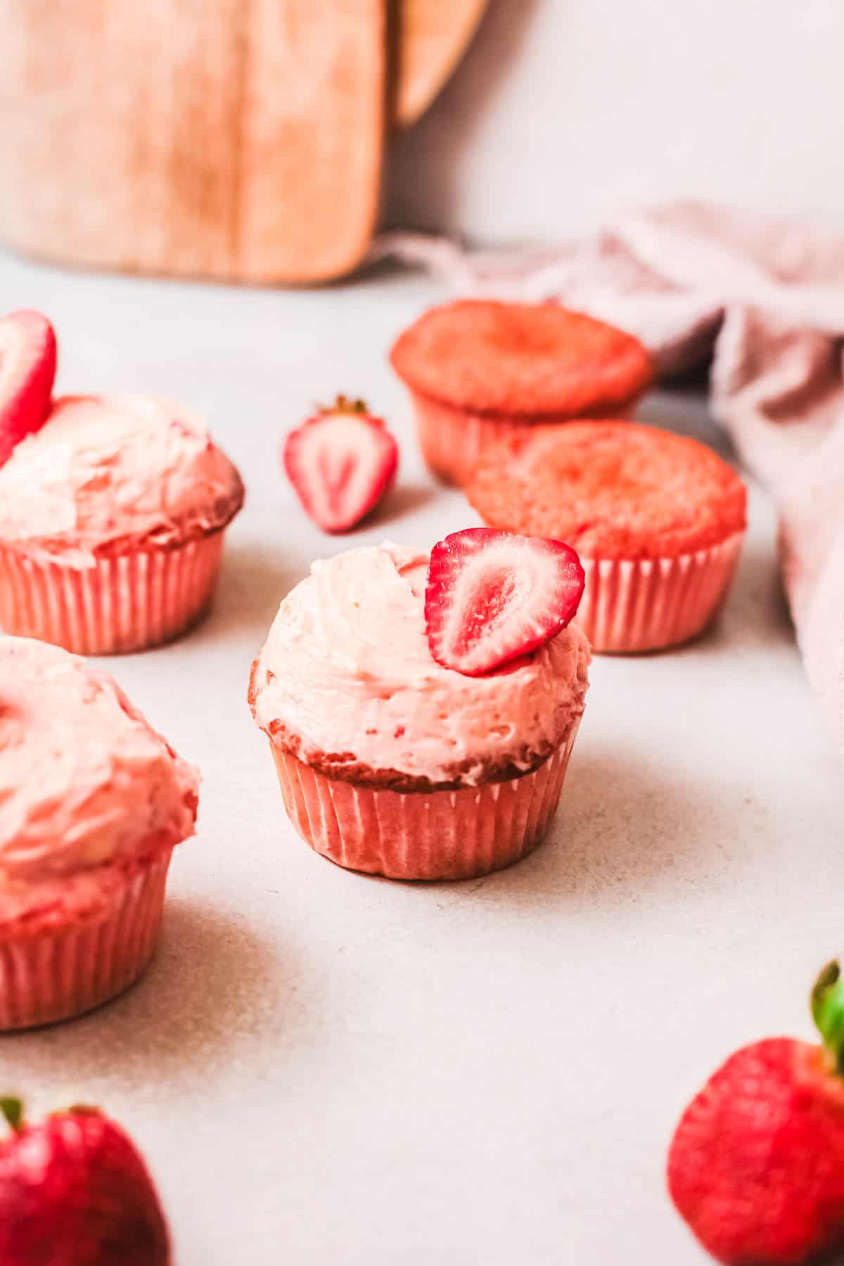 Strawberry cupcake frosted with sliced strawberry on top on white counter.