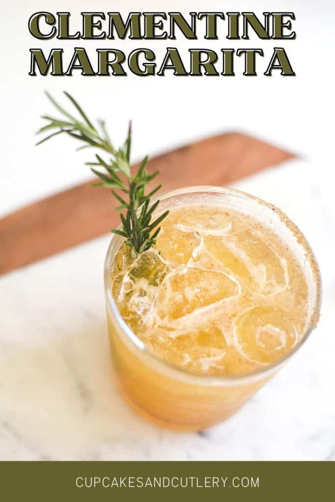 Clementine margarita in a glass garnished with a rosemary sprig on a white marble board.