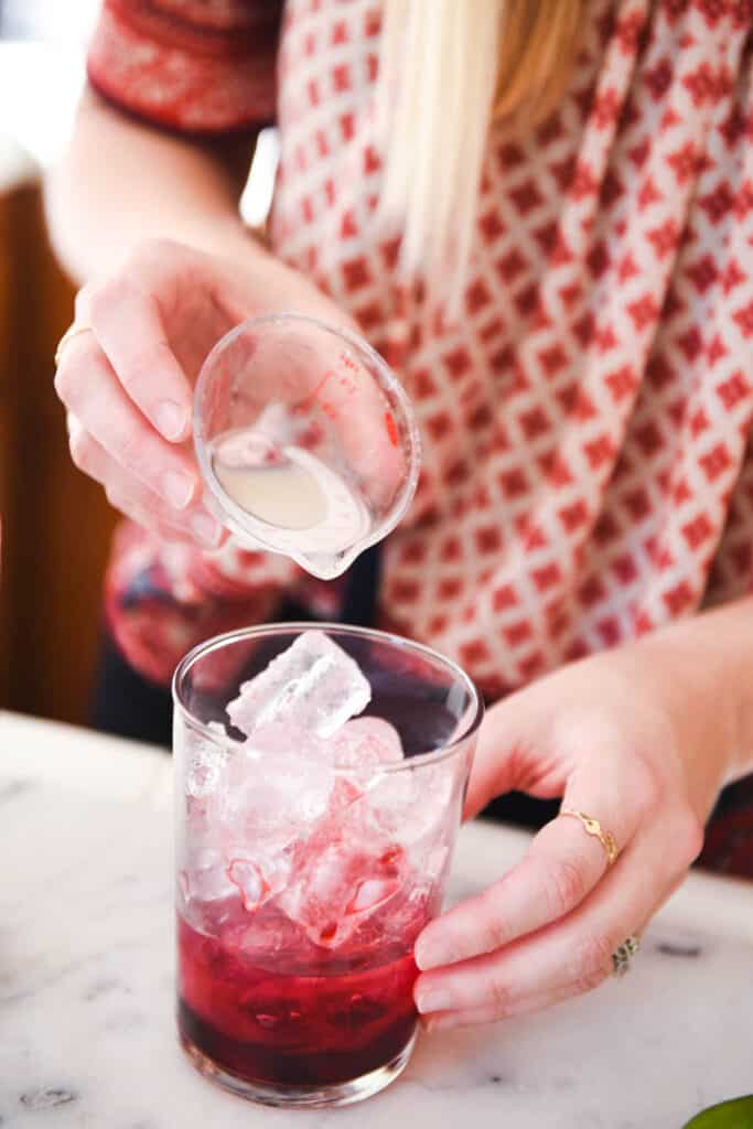 A woman adding fresh lime juice to a cocktail glass with ice.