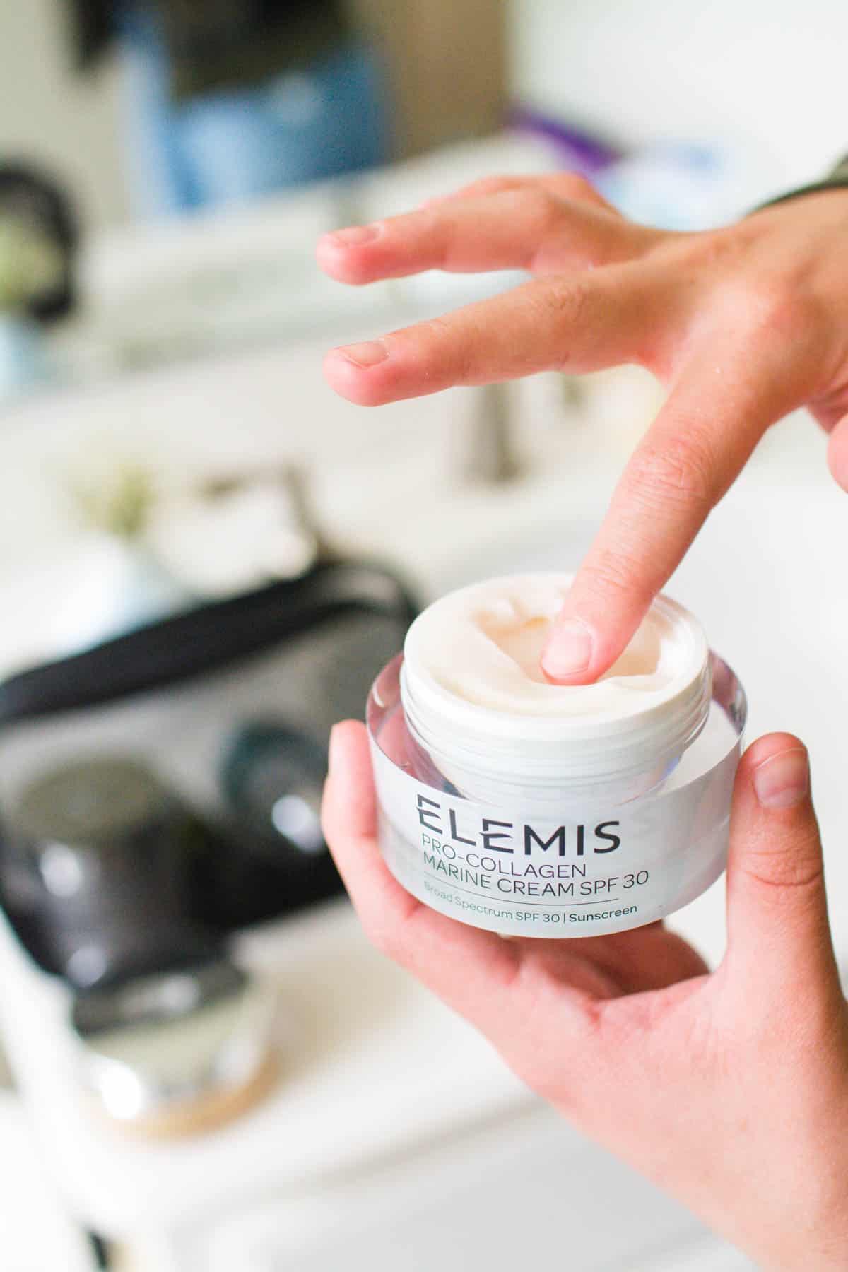 Hands holding a jar of Elemis Pro-Collagen Marine Cream with spf 30 and dipping her finger in.
